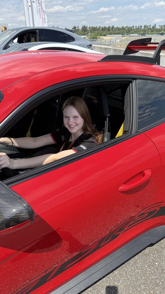 Lächelnde junge Frau am Steuer eines roten Porsche GT3 RS an der Rennstrecke