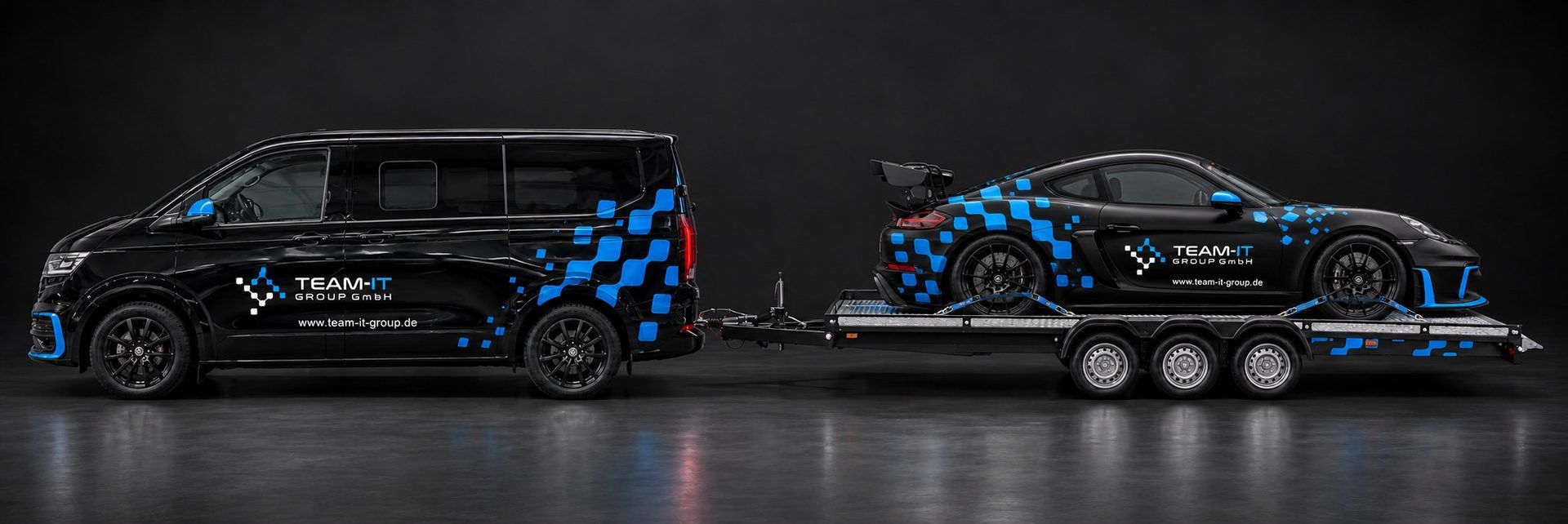 Gespann aus schwarzem VW T7, offenem Anhänger und dem 718 Cayman GT4 im Team-IT-Design
