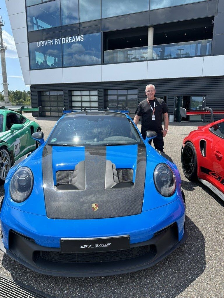 Teammitglied vor einem blauen Porsche GT3 RS an einer Rennstrecke